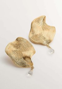 Pendientes ondulados en tono dorado con textura estriada y acentos de cristal transparente colgantes. La forma orgánica única añade dimensión e interés visual.