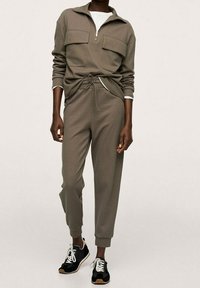 Conjunto deportivo gris que incluye una sudadera de forro polar con cremallera y dos bolsillos delanteros, y pantalones deportivos ajustados a juego. Combinado con zapatillas negras.