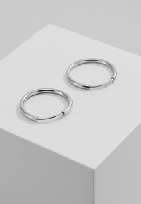 Pendientes de aro de metal plateado con un diseño circular y suave, y una pequeña apertura en el aro para el cierre. Acabado minimalista y pulido.