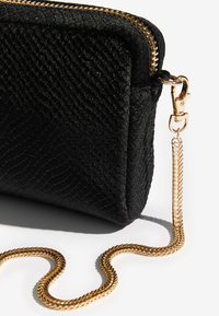 Borsetta clutch nera con texture effetto pelle di serpente, ferramenta color oro e tracolla a catena intrecciata. Chiusura con cerniera in alto.
