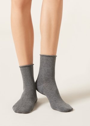 Two bare legs wearing plain mid-calf grey socks standing on a neutral, light background.