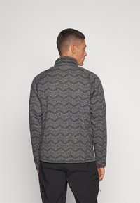 Gray, textured fleece jacket featuring a zigzag pattern, high collar, and zip closure, paired with black pants.