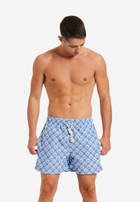 Costumi da bagno blu con motivo geometrico e accenti bianchi, dotati di vita elastica e chiusura con cordoncino. Tessuto leggero.