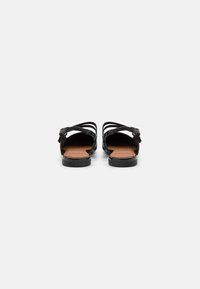 Black leather sandals with crisscross straps, flat sole, and a padded insole. Smooth texture with subtle sheen and adjustable ankle strap.