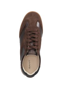 Brown sneaker featuring suede and leather materials, round toe, lace-up design, and logo on the tongue. Flat rubber sole visible inside.