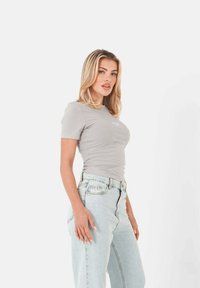 Lichtgrijze t-shirt met korte mouwen, voorzien van een aansluitende pasvorm en een ronde halslijn, gecombineerd met hoge taille lichtblauwe denim jeans.