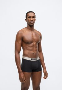 Fekete boxeralsó arany színű elasztikus derékpánttal, amelyen a Diesel logó szerepel. A modell tónusos testalkatú, semleges háttér előtt áll.