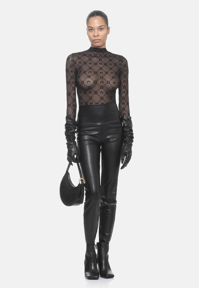 Top lungo a manica trasparente nera con un motivo floreale, pantaloni in pelle nera a vita alta, guanti neri e una borsa strutturata. Stivaletti completano il look.