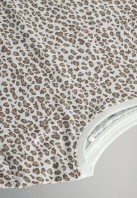 Top con estampado de leopardo en tejido suave, que presenta una base blanca y manchas marrones. Escote redondeado con acentos marfil, que destaca el diseño casual.