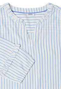 Blouse blanche avec de fines rayures verticales bleues, un petit col en V, et des poignets élastiques froncés aux manches longues.