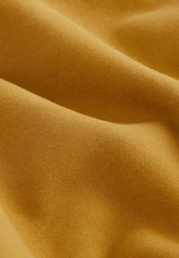 Tissu d'un jaune moutarde chaud, caractérisé par une texture douce et lisse avec un motif de tricot fin, créant de douces ondulations dans le textile.
