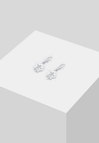 Sølvstjernede øreringe med et lagdelt design, der har en poleret overflade og krog-lukninger, præsenteret på en hvid geometrisk pedestal.