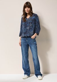 Marinblus med mönster i geometriska former, kombinerad med ljusblå vida jeans och vita sneakers. Strukturerad tyg och avslappnad passform.