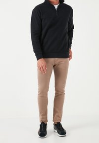 Felpa nera con zip, pantaloni beige slim-fit e sneakers nere con suola bianca. Tessuto morbido, design casual e silhouette aderente.