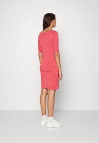Vestido justo vermelho com mangas curtas, padrão de bolinhas, costas à descoberta e um pequeno detalhe de botão. Combinado com ténis brancos.