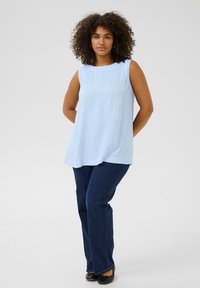 Haut sans manches bleu clair avec un col rond, associé à un jean évasé bleu foncé et des chaussures plates noires. Tissu lisse, design décontracté.