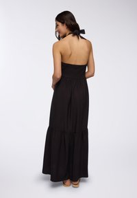 Abito maxi senza maniche di colore nero con busto arricciato, orlo arricciato e chiusura a cravatta sulla parte posteriore. Tessuto morbido, lunghezza alla caviglia.