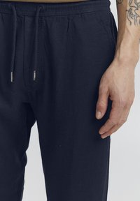 Mörkblå linnebyxor med elastisk midja och dragsko. Har raka ben och en texturerad tygfinish.