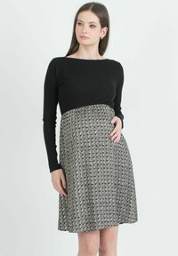 Musta ribbed pitkähihainen paita, jossa on kuvioitu hame, jossa on vuorotellen harmaita ja kermaisia ympyröitä, tiukka yläosa ja liehuva helma.