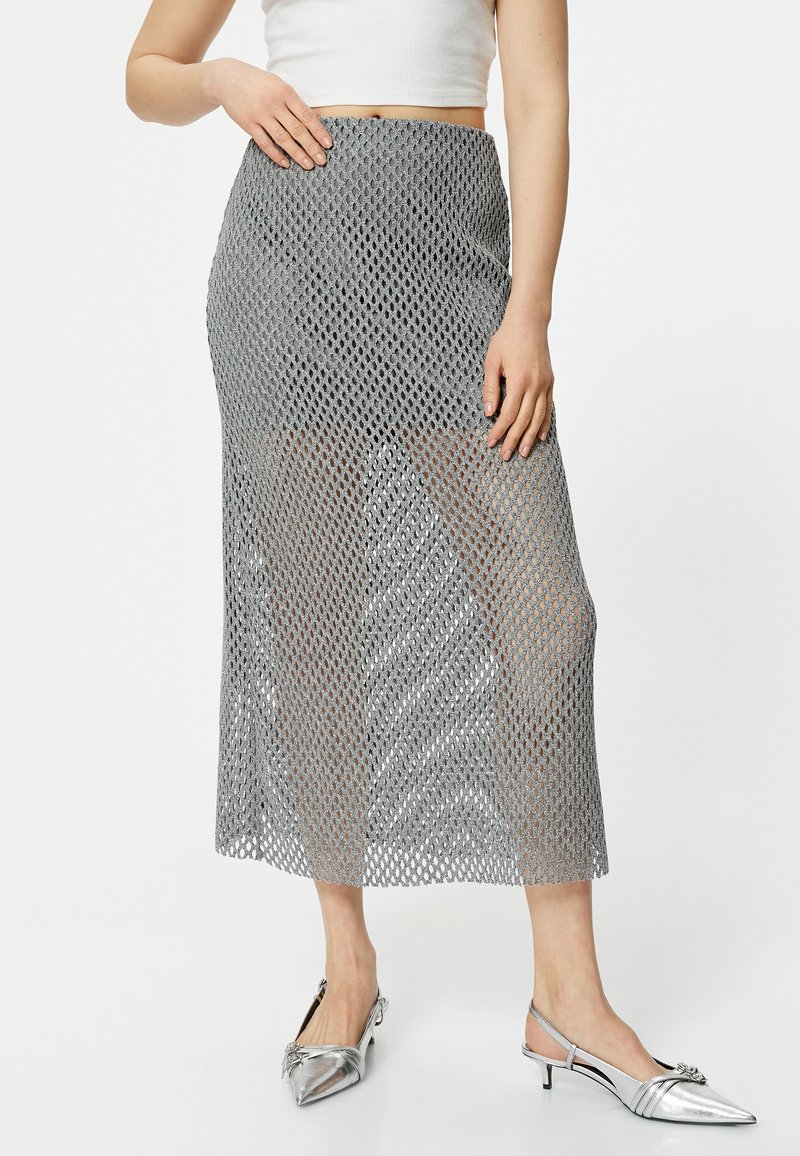 Grå mesh nederdel med diamantmønster, mid-længde, med en tætsiddende talje. Parret med sølvfarvede slingback sko med spidse tæer.