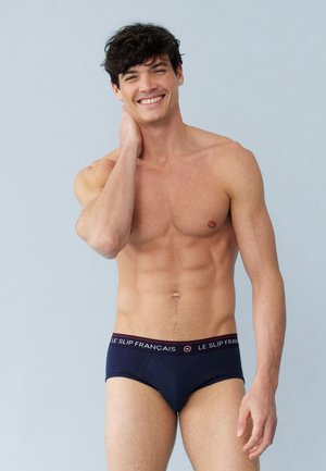 Caleçons pour hommes bleu marine avec une ceinture texturée arborant "LE SLIP FRANÇAIS" en blanc et rouge. Le vêtement a une coupe ajustée et un tissu lisse.