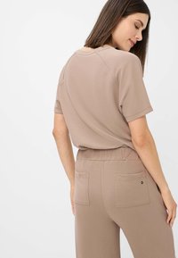 Top marrone a maniche corte con scollo rotondo. Tessuto morbido con una superficie liscia. Presenta una vestibilità comoda e dettagli cuciti sulle spalle.