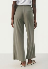 Pantalon large en tissu vert olive, avec une texture lisse, une taille élastique et une coupe ample qui tombe jusqu'au sol.