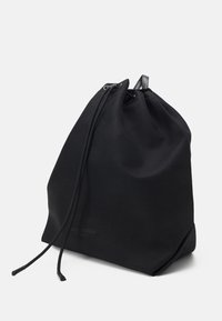 Sac à dos noir à cordon de serrage en toile avec une texture lisse et une forme arrondie. Présente des accents en cuir et un marquage subtil à la base.