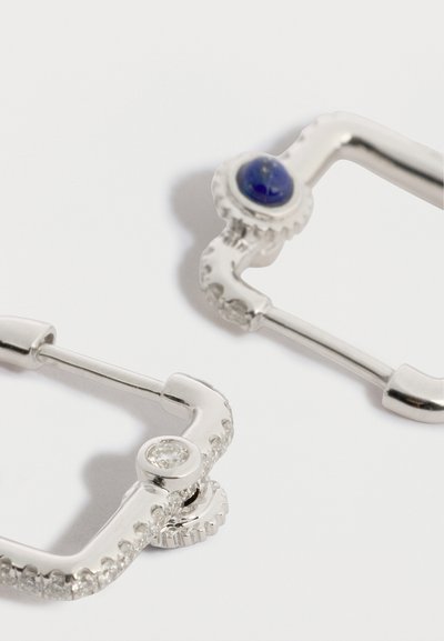 Cercei din argint cu formă pătrată, cu o piatră albastră și un accent de piatră prețioasă transparentă. Design texturat pe margini. Închidere modernă cu clemă.