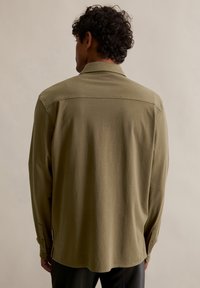 Langarmshirt van olijfgroen stof, met een grote kraag, knoopsluitingen bij de manchetten en een rechte zoom met een rugnaad ontwerp.