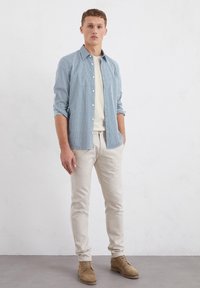 Light blue patterned button-up shirt, cream t-shirt, light beige trousers, and tan suede shoes. Simple design with a relaxed fit.