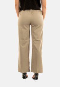 Pantaloni beige a gamba larga con vita elastica, tessuto liscio e tasche laterali, abbinati a scarpe nere con tacco alto.