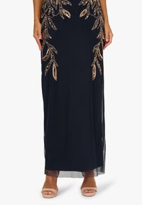 Navy Maxi-Kleid mit aufwendiger rosegoldener Blattstickerei, transparenten Seiten und fließender Silhouette, kombiniert mit nudefarbenen Schnürsandalen.