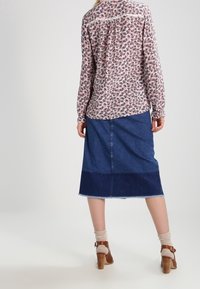 Blomstrete skjorte med lange ærmer og knap-ned ryg, parret med en mørk denimskørt med en lysere syet kant og brune hælede sandaler.
