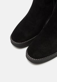 Botas de tobillo de ante negro con punta redondeada, presentan costuras visibles a lo largo de la suela y una suela de goma texturizada para mayor agarre.