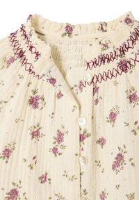 Floral blouse with a cream background, featuring purple roses and green leaves. Smocked neckline with burgundy accents and three white buttons.