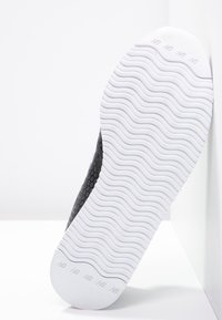 Botte de sport noire avec une tige texturée et une semelle en caoutchouc blanche et ondulée. Présente un logo sur le talon et un design de capuchon lisse.