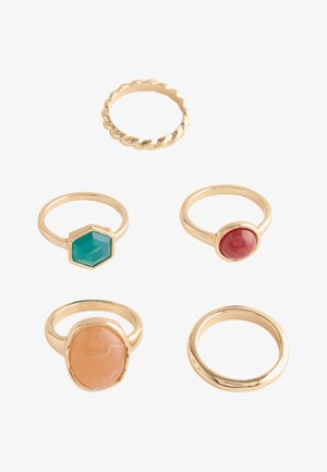 Five gold rings with different designs including twisted band, plain band, and bands with red, green hexagon, and large oval beige stones.