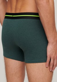 Teal boxershorts met een zwarte tailleband met een groene accentstreep. Gemaakt van een zachte, gestructureerde stof, hebben ze een aansluitende pasvorm.