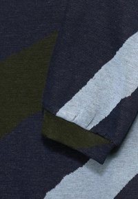 Zbliżenie na dzianinę w ciemnoniebieskie, jasnoniebieskie i oliwkowozielone geometryczne paski oraz mankiet z zagięciem.