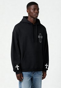 Felpa nera con cappuccio realizzata in tessuto morbido, dotata di tasca frontale, logo bianco e disegni a croce sulle maniche. Fit casual e rilassato.