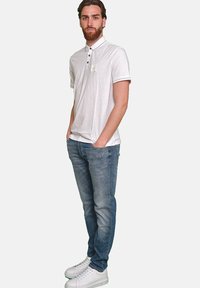 Weißes Poloshirt mit Kragen, schwarzen Akzenten und Logo auf der linken Brust. Getragen mit hellblauen Slim-Fit-Jeans und weißen Sneakers.