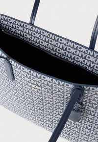 Niebiesko-biała torba na ramię z powtarzającym się wzorem logo, materiał tkaninowy, dwa uchwyty oraz wewnętrzna kieszeń na zamek.