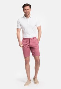 Shorts en coton rose clair avec une coupe décontractée, présentant une fermeture à bouton et des poches. Associés à un polo blanc ajusté et des mocassins beige.