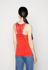 Camiseta roja sin mangas con un diseño de espalda de encaje. Tejido suave, con escote redondo y un cierre de botón en la parte posterior.