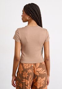 T-shirt marron ajusté à manches courtes en tissu doux, avec un col rond et une texture lisse, associé à un pantalon marron à motifs floraux.