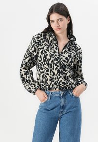 Pullover in fleece nero e crema con texture, dotato di colletto a mezzo zip, caratterizzato da una stampa leopardata e un design cropped. Indossato con jeans blu.