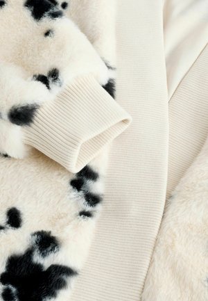 Faux fur jacket featuring a cream base with black spots, ribbed cuffs, and a soft texture. The fabric has a plush, cozy appearance.