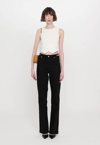 White cropped tank top with a wavy hem, paired with high-waisted black flared jeans, and a small orange handbag with a chain strap.