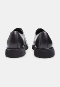  Scarpe in pelle nera con finitura liscia, punta rotonda e suola in gomma a contrasto. Dettaglio di cucitura sottile sul retro.